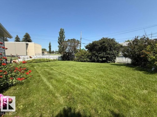Expansive grassy yard with mature shrubs and trees, framed by a white picket fence - 9908 96A Avenue, Fort Saskatchewan, AB - Outdoor