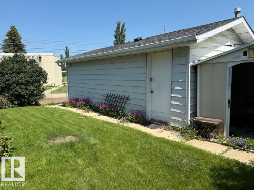 Manicured lawn with a detached auxiliary structure featuring a shingled roof, horizontal siding, and an access door - 9908 96A Avenue, Fort Saskatchewan, AB - Outdoor