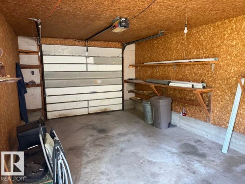 Garage space featuring a roll-up door, concrete flooring, exposed chipboard walls, and built-in shelving - 9908 96A Avenue, Fort Saskatchewan, AB - Indoor Photo Showing Garage