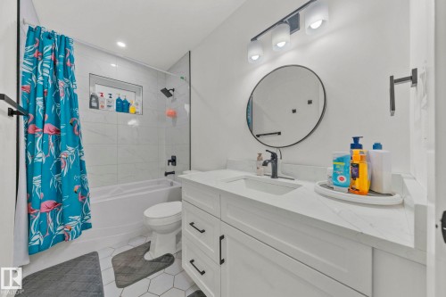 Bathroom featuring a white vanity with an integrated sink, black faucet, and a round mirror - 4119 18 Avenue Nw, Edmonton, AB - Indoor Photo Showing Bathroom