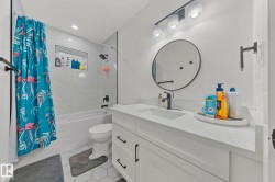 Bathroom featuring a white vanity with an integrated sink, black faucet, and a round mirror - 