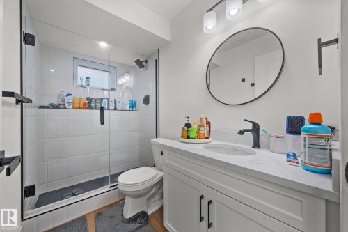 Modern bathroom featuring a glass-enclosed shower with white subway tile, a vanity with a white countertop and integrated sink, a circular framed mirror, and matte black fixtures - 4119 18 Avenue Nw, Edmonton, AB - Indoor Photo Showing Bathroom