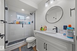 Modern bathroom featuring a glass-enclosed shower with white subway tile, a vanity with a white countertop and integrated sink, a circular framed mirror, and matte black fixtures - 