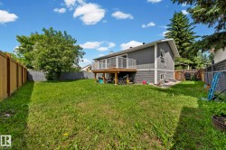 Spacious rear yard featuring a large wooden deck with white railings, grey siding exterior, a privacy fence, and mature perimeter trees - 