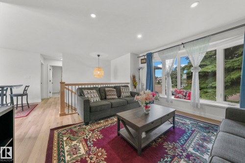 Bright living space featuring large bay windows, wood-finish flooring, recessed lighting, a modern ceiling pendant, and an open railing - 4119 18 Avenue Nw, Edmonton, AB - Indoor Photo Showing Living Room