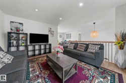 Open-concept living space with light wood-finish flooring, recessed lighting, and a modern wood and iron railing - 