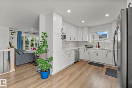 Kitchen featuring white cabinetry with dark hardware, a white tile backsplash, stainless steel dishwasher, and wood-finish flooring - 4119 18 Avenue Nw, Edmonton, AB - Indoor Photo Showing Kitchen