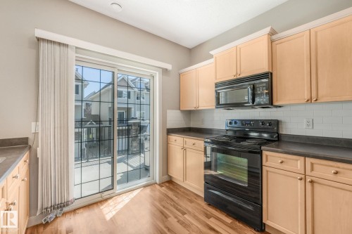 Kitchen featuring wood-finish flooring, light wood cabinetry, dark countertops, white subway tile backsplash, and a black range with an overhead microwave - #16 7293 South Terwillegar Dr Nw, Edmonton, AB - Indoor Photo Showing Kitchen
