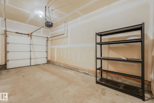 Garage interior featuring a concrete floor, light-toned walls, overhead lighting, and a rolling garage door with an automatic opener - #16 7293 South Terwillegar Dr Nw, Edmonton, AB - Indoor Photo Showing Garage