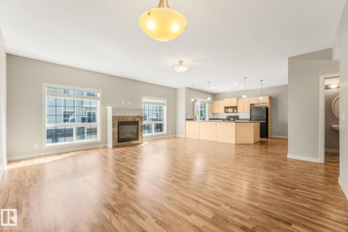 Open-concept living space featuring wood-finish flooring, a stone-surround fireplace, and large windows - #16 7293 South Terwillegar Dr Nw, Edmonton, AB - Indoor With Fireplace