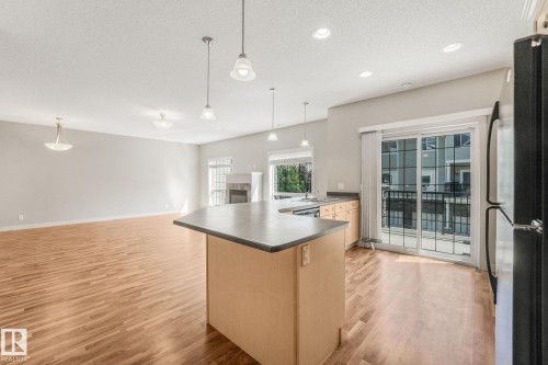 Open-concept living space featuring wood-finish flooring, a central kitchen island with countertop, and a built-in fireplace - #16 7293 South Terwillegar Dr Nw, Edmonton, AB - Indoor