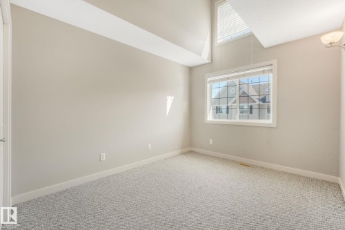 Room featuring a large window with white blinds, high vaulted ceilings, and light-toned carpet flooring - #16 7293 South Terwillegar Dr Nw, Edmonton, AB - Indoor Photo Showing Other Room