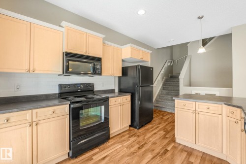 Kitchen featuring natural wood-finish cabinetry, dark countertops, and a white subway tile backsplash - #16 7293 South Terwillegar Dr Nw, Edmonton, AB - Indoor Photo Showing Kitchen