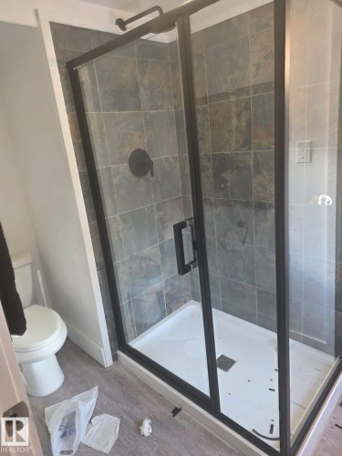 Glass-enclosed shower with matte black fixtures, stone-finish tile surround, and a white shower pan - 10656 93 Street, Edmonton, AB 