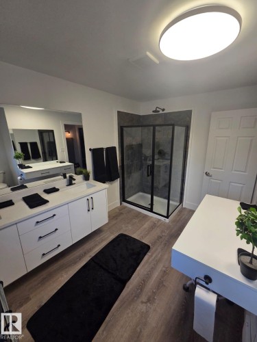 Modern bathroom featuring a corner shower with dark-framed glass enclosure, stone-look tile shower surround, and a wall-mounted shower head - 10656 93 Street, Edmonton, AB 