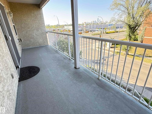 Spacious balcony featuring a textured stucco exterior, white metal railing, and durable concrete flooring - #302 8215 84 Av Nw, Edmonton, AB - Outdoor With Balcony With Exterior