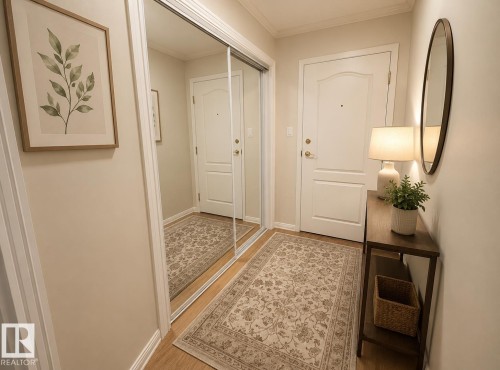 Entryway featuring wood-finish flooring, a white paneled door with brass hardware, and a mirrored closet with sliding doors - #302 8215 84 Av Nw, Edmonton, AB - Indoor Photo Showing Other Room