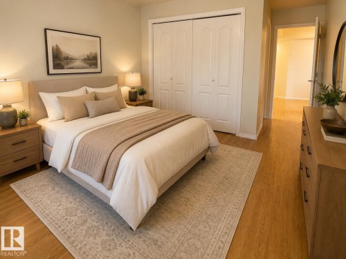 Spacious bedroom featuring wood-finish flooring, a neutral upholstered headboard, and a double bi-fold closet with white paneled doors - #302 8215 84 Av Nw, Edmonton, AB - Indoor Photo Showing Bedroom