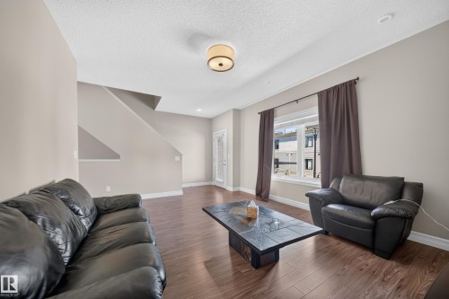 Spacious living area featuring wood-finish flooring, neutral wall tones, a large window, and recessed lighting - #100 804 Welsh Dr Sw, Edmonton, AB - Indoor Photo Showing Living Room