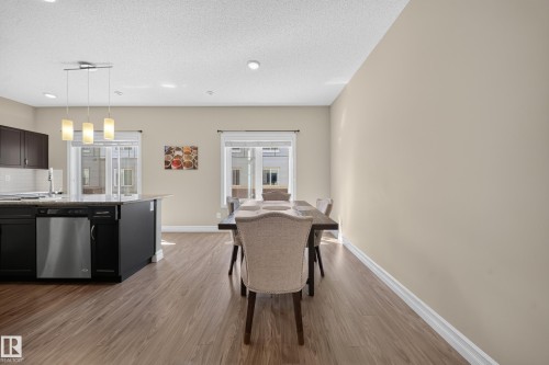 Open-concept kitchen and dining area featuring wood-finish flooring, dark cabinetry, and light-toned walls - #100 804 Welsh Dr Sw, Edmonton, AB - Indoor