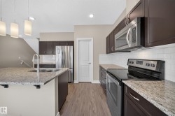Modern kitchen featuring dark wood cabinetry, light granite countertops, stainless steel appliances, and wood-finish flooring - 