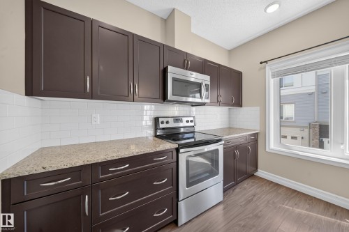 Kitchen featuring dark wood cabinetry, light-toned countertops, white subway tile backsplash, and stainless steel appliances - #100 804 Welsh Dr Sw, Edmonton, AB - Indoor Photo Showing Kitchen With Stainless Steel Kitchen