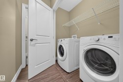 Dedicated laundry space featuring a front-load washer and dryer, wood-finish flooring, neutral-toned walls, and a wire storage shelf - 