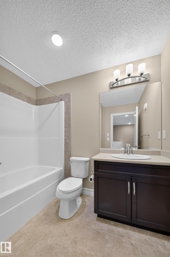 Bathroom featuring a combined tub and shower unit with tile surround, a dark wood-finish vanity with a light countertop, an undermount sink, and tile flooring - #100 804 Welsh Dr Sw, Edmonton, AB - Indoor Photo Showing Bathroom