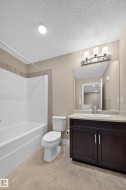 Bathroom featuring a combined tub and shower unit with tile surround, a dark wood-finish vanity with a light countertop, an undermount sink, and tile flooring - 