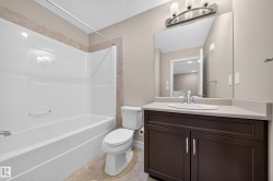 Bathroom featuring a white tub-shower combination with a tiled surround, a toilet, a dark wood-finish vanity with a light countertop, an undermount sink, and a large wall-mounted mirror - 