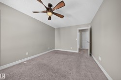 Spacious room featuring neutral paint tones, plush carpeting, a multi-blade ceiling fan with integrated lighting, and white baseboards - 
