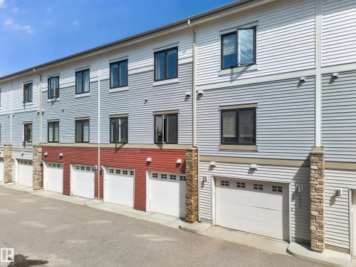 Modern multi-level townhome exteriors featuring horizontal siding in white and gray tones, red accent siding, and stone pillar details - #100 804 Welsh Dr Sw, Edmonton, AB - Outdoor With Exterior