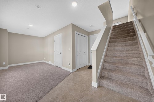 Carpeted staircase with white railings, tile flooring, and neutral wall tones - #100 804 Welsh Dr Sw, Edmonton, AB - Indoor Photo Showing Other Room