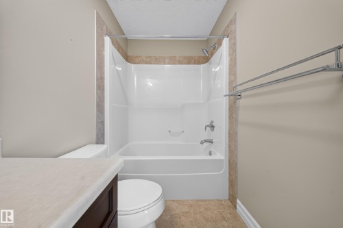 Bathroom featuring a white tub/shower combination with chrome fixtures, surrounded by a tiled accent wall - #100 804 Welsh Dr Sw, Edmonton, AB - Indoor Photo Showing Bathroom