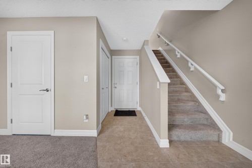 Foyer featuring neutral wall tones, white trim, and a carpeted staircase with white handrails - #100 804 Welsh Dr Sw, Edmonton, AB - Indoor Photo Showing Other Room