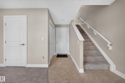 Foyer featuring neutral wall tones, white trim, and a carpeted staircase with white handrails - 