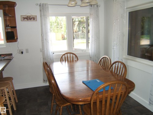 Dining area featuring a wood-finish table, multiple windows, a built-in wood-finish corner shelf, and dark-toned flooring - 151042 Twp  Rd 562, Rural Two Hills County, AB - Indoor Photo Showing Dining Room