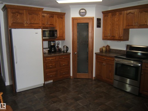 Kitchen featuring wood-finish cabinetry, dark countertops, and tile-style flooring - 151042 Twp  Rd 562, Rural Two Hills County, AB - Indoor Photo Showing Kitchen