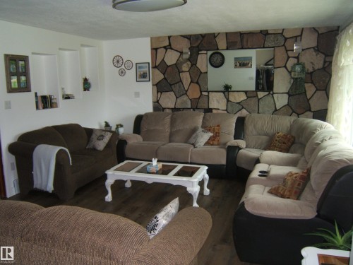 Spacious interior featuring a stone-accented wall, wood-finish flooring, built-in wall niches, a large wall mirror, and ceiling-mounted lighting - 151042 Twp  Rd 562, Rural Two Hills County, AB - Indoor Photo Showing Living Room