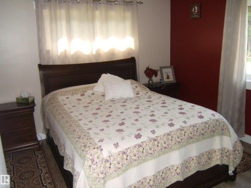 Interior space featuring wood-finish flooring, a window with sheer curtains, an accent wall with a deep red finish, and white painted walls - 151042 Twp  Rd 562, Rural Two Hills County, AB - Indoor Photo Showing Bedroom