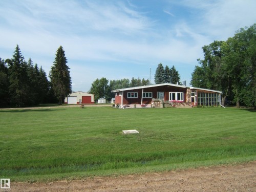 Ranch-style residence featuring a prominent red facade with stone accents, a full-length sunroom, and a spacious front lawn - 151042 Twp  Rd 562, Rural Two Hills County, AB - Outdoor