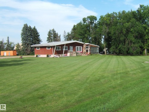 Expansive green lawn surrounds a single-story home featuring red siding, stone facade accents, and multiple windows - 151042 Twp  Rd 562, Rural Two Hills County, AB - Outdoor