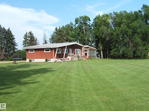 Expansive green lawn bordering a one-story residence with red siding and a stone facade section - 151042 Twp  Rd 562, Rural Two Hills County, AB - Outdoor