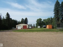 Gravel driveway with a large metal workshop featuring a roll-up door and side entry - 