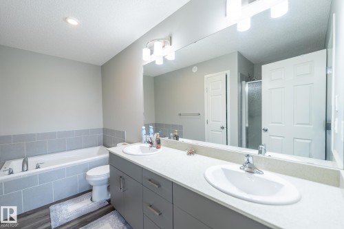 Bathroom featuring a dual-sink vanity with light-colored countertops, an integrated bathtub with light gray tile surround, and wood-finish flooring - 5403 Lark Landing Nw, Edmonton, AB - Indoor Photo Showing Bathroom