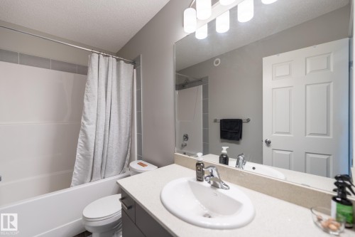 Contemporary bathroom featuring a white porcelain sink with chrome faucet, light-toned countertop, and modern vanity lighting - 5403 Lark Landing Nw, Edmonton, AB - Indoor Photo Showing Bathroom