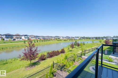 Balcony with black railing and glass panels overlooking a tranquil body of water, bordered by green spaces and mature landscaping - 5403 Lark Landing Nw, Edmonton, AB - Outdoor With Body Of Water With View