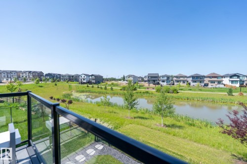 Private balcony featuring glass railings and composite decking, overlooking a tranquil pond with surrounding green spaces and residential properties - 5403 Lark Landing Nw, Edmonton, AB - Outdoor With View