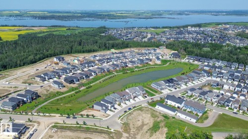 Aerial perspective showcasing a developing residential community featuring a central pond, established green spaces, and a variety of contemporary-style homes - 5403 Lark Landing Nw, Edmonton, AB - Outdoor With View