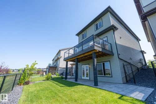 Rear exterior featuring a second-story balcony with glass railing, ground-level patio with pavers, and a green lawn - 5403 Lark Landing Nw, Edmonton, AB - Outdoor